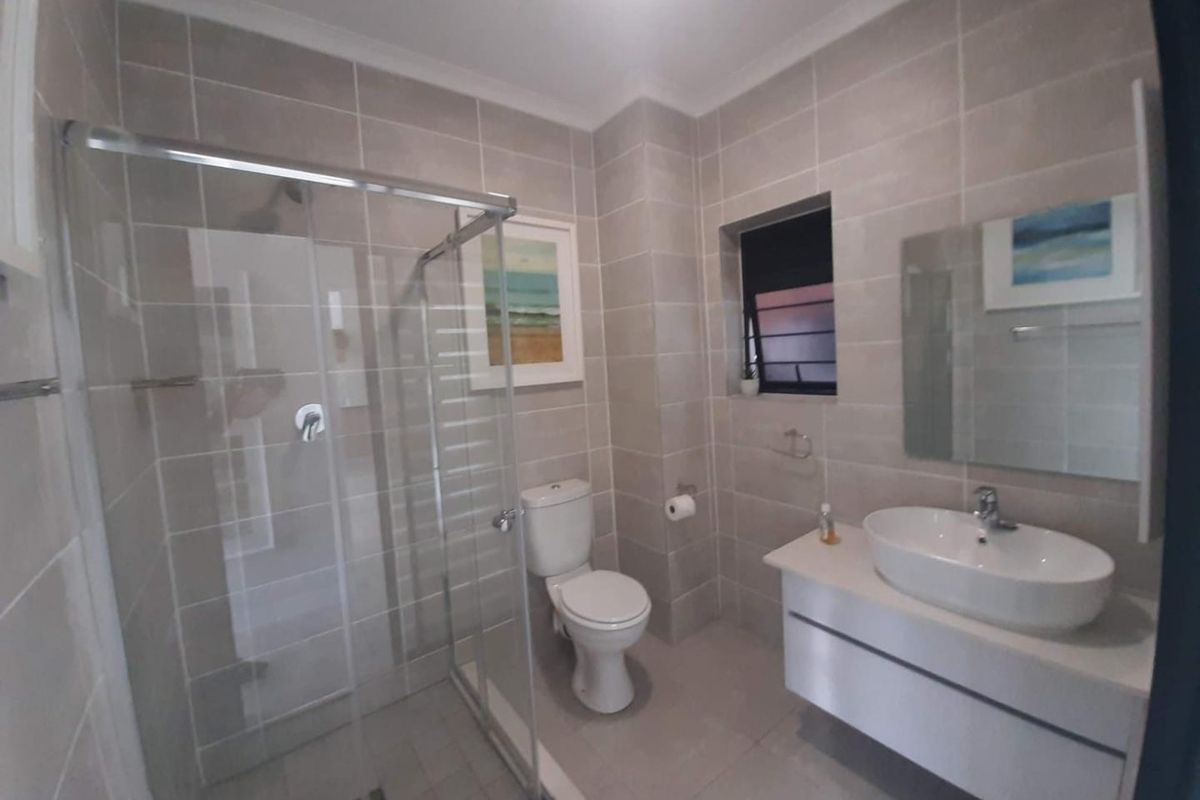 Modern bathroom featuring a glass-enclosed shower, wall-mounted vanity with a vessel sink, and neutral floor-to-ceiling tiling.