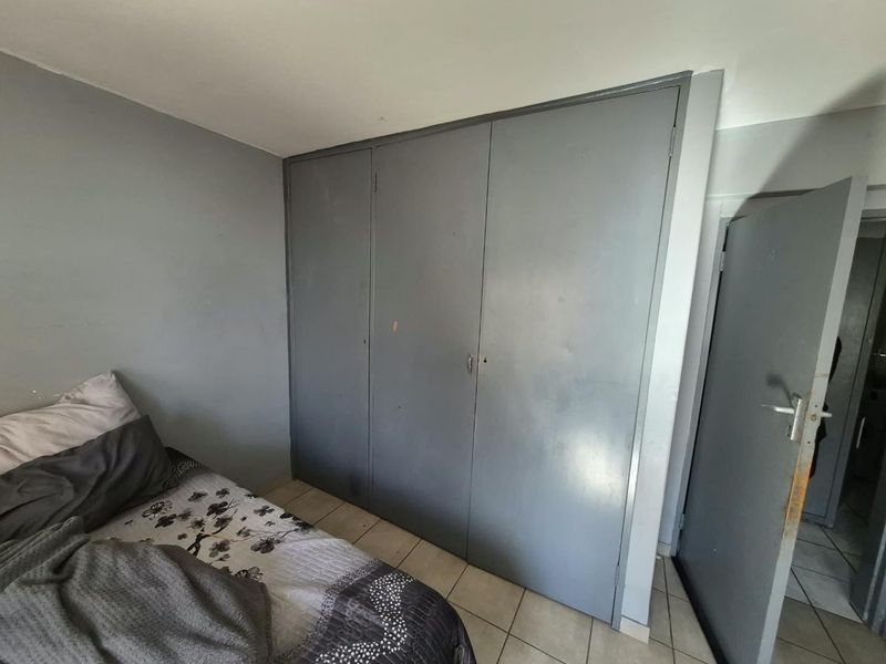 A bedroom featuring built-in wardrobes and tiled flooring, showing signs of wear and requiring cosmetic updates.