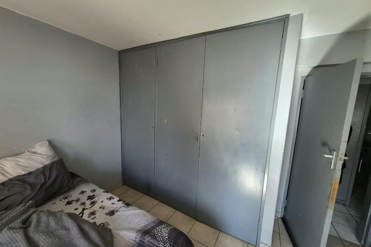 A bedroom featuring built-in wardrobes and tiled flooring, showing signs of wear and requiring cosmetic updates.