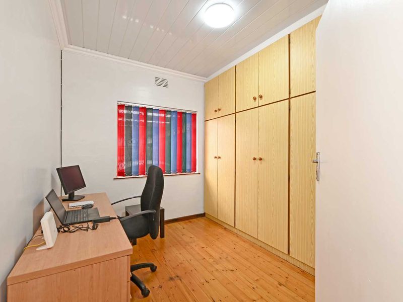 A bedroom featuring timber flooring, built-in cupboards, and a tongue and groove ceiling, currently utilized as a home office space.