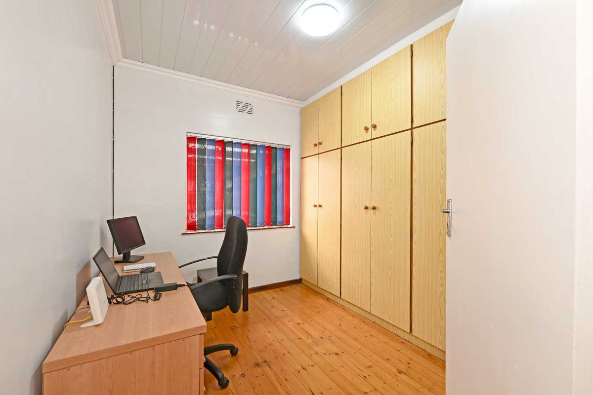 A bedroom featuring timber flooring, built-in cupboards, and a tongue and groove ceiling, currently utilized as a home office space.