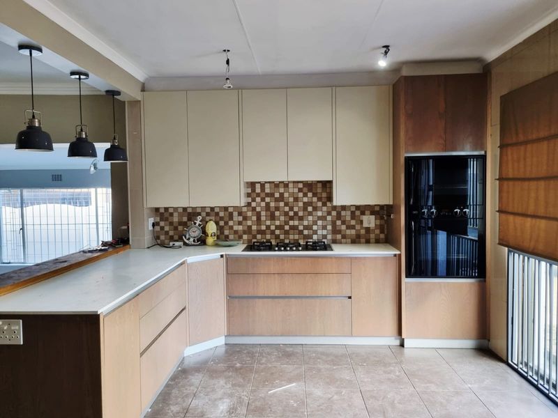 Modern kitchen featuring wood-tone and cream cabinetry, stone countertops, built-in oven, gas hob, and a decorative mosaic tiled backsplash.