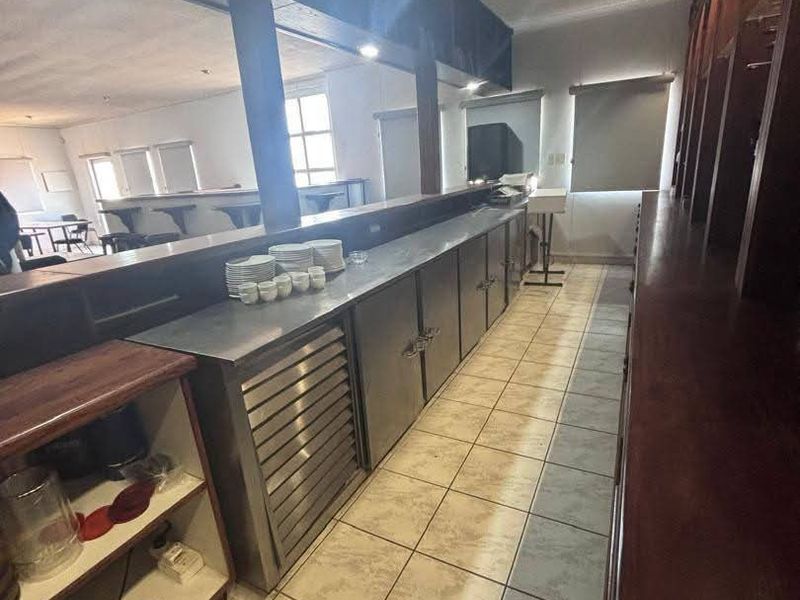 A functional bar area featuring stainless steel under-counter refrigeration, durable countertops, and built-in wooden cabinetry with tiled flooring.