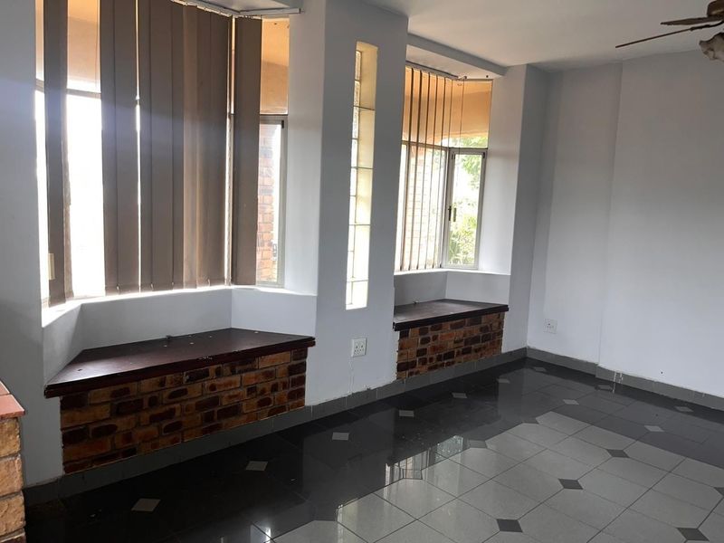 An empty living area featuring unique brick-faced window seats, glass block accents, and dark tiled flooring with a ceiling fan.