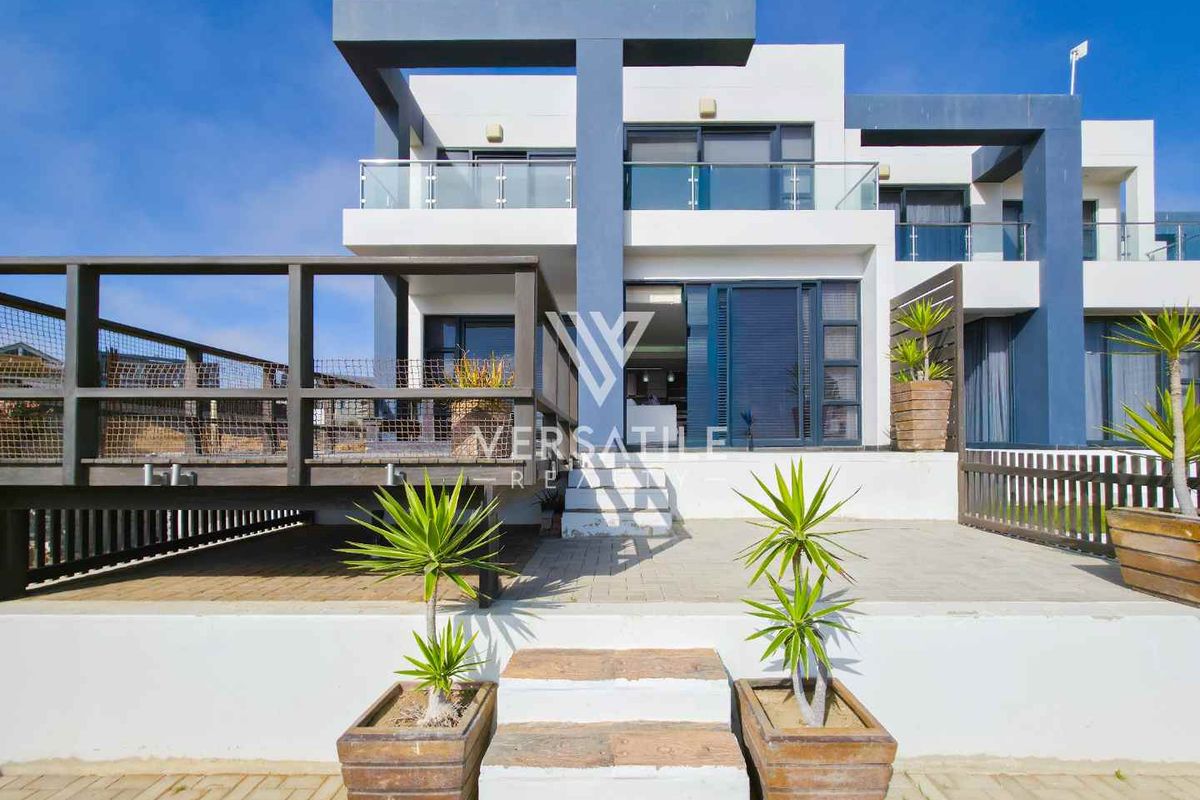 Modern two-story townhouse exterior featuring a raised timber deck, paved patio area, glass balustrades, and contemporary architectural facade.