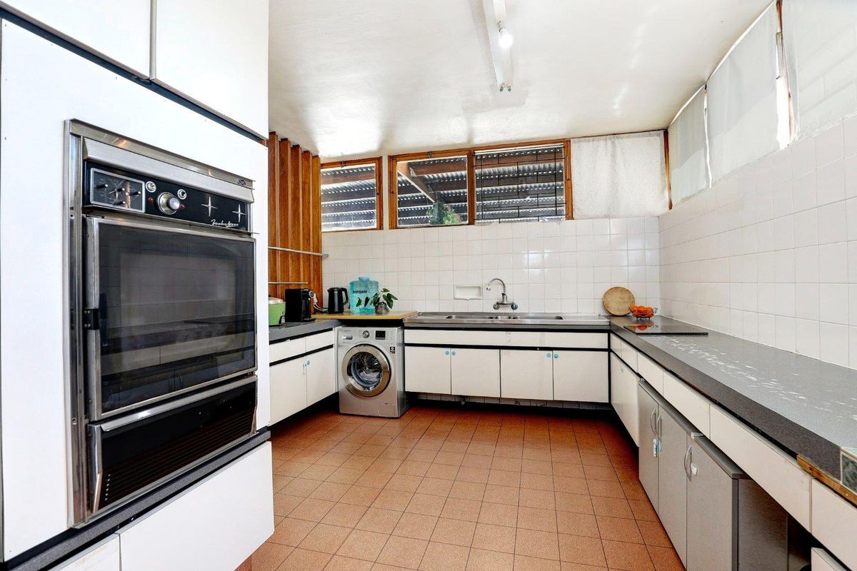 A functional kitchen featuring built-in cabinetry, a wall-mounted oven, integrated sink, and space for laundry appliances with tiled flooring.