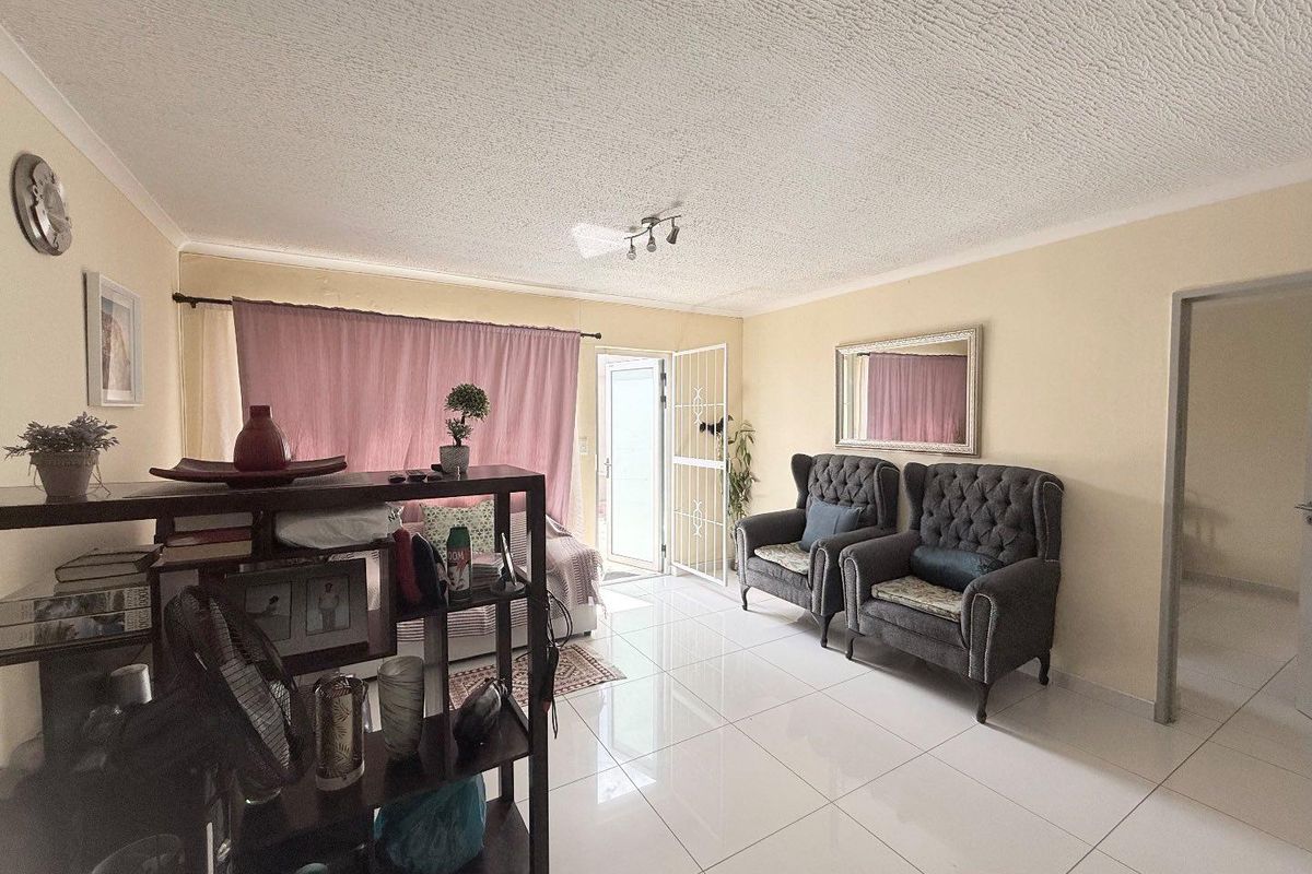 A bright living room featuring polished floor tiles, a textured ceiling, and direct access to an outdoor area through a security gate.