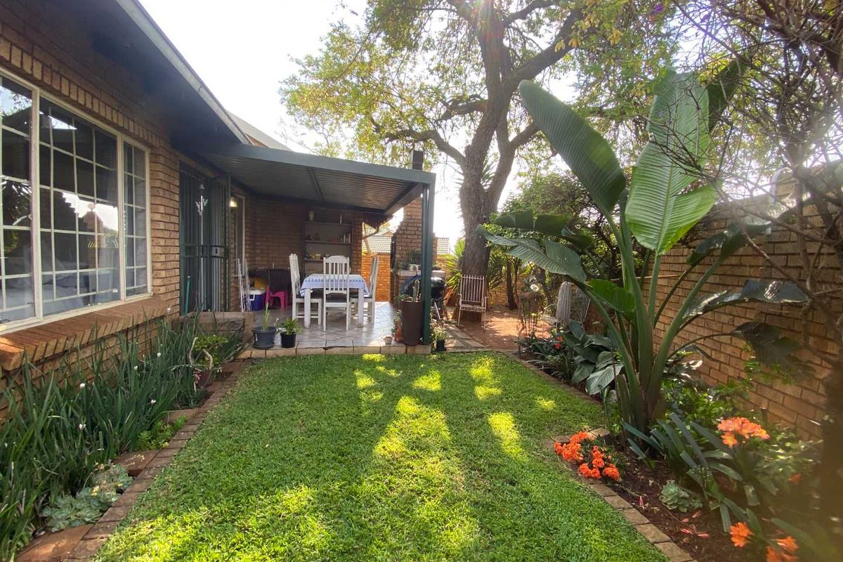 A private rear garden featuring a covered patio area, established landscaping, and brick boundary walls, providing a pleasant outdoor living space.