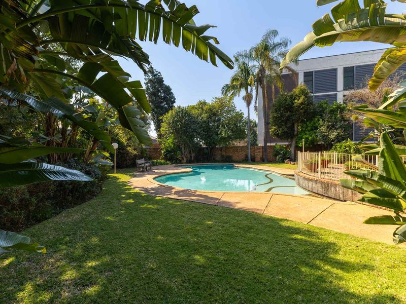 A private outdoor pool area featuring a landscaped garden, paved surround, and established trees, providing a tranquil space for relaxation.