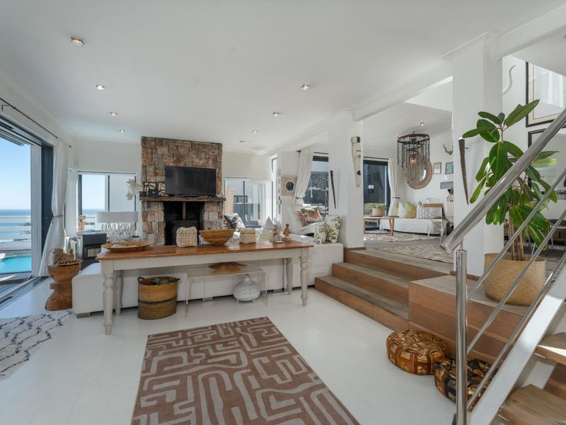 Spacious open-plan living area featuring a stone fireplace, timber staircase with stainless steel balustrade, and seamless flow to an outdoor deck with ocean views.