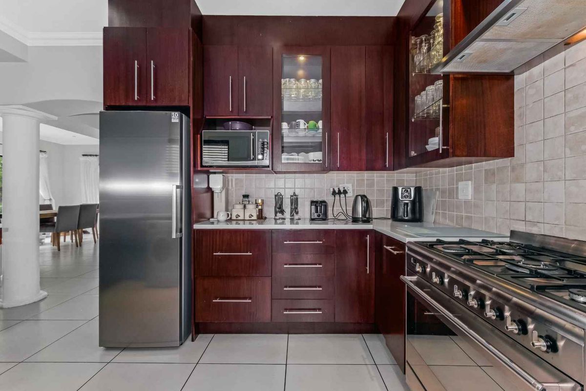 A functional kitchen featuring dark wood cabinetry, tiled backsplash, stainless steel gas range, and integrated microwave, with tiled flooring throughout.