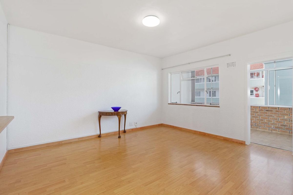 A bright, empty bedroom featuring laminate flooring, neutral walls, and a window with access to an adjacent balcony area.