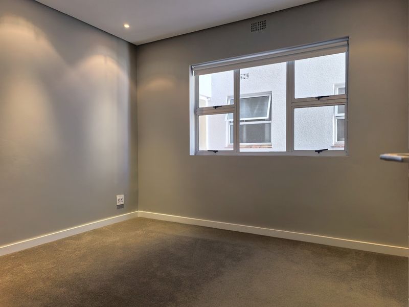 A clean, empty bedroom featuring neutral grey walls, plush carpeting, and modern aluminium-framed windows with integrated ventilation.