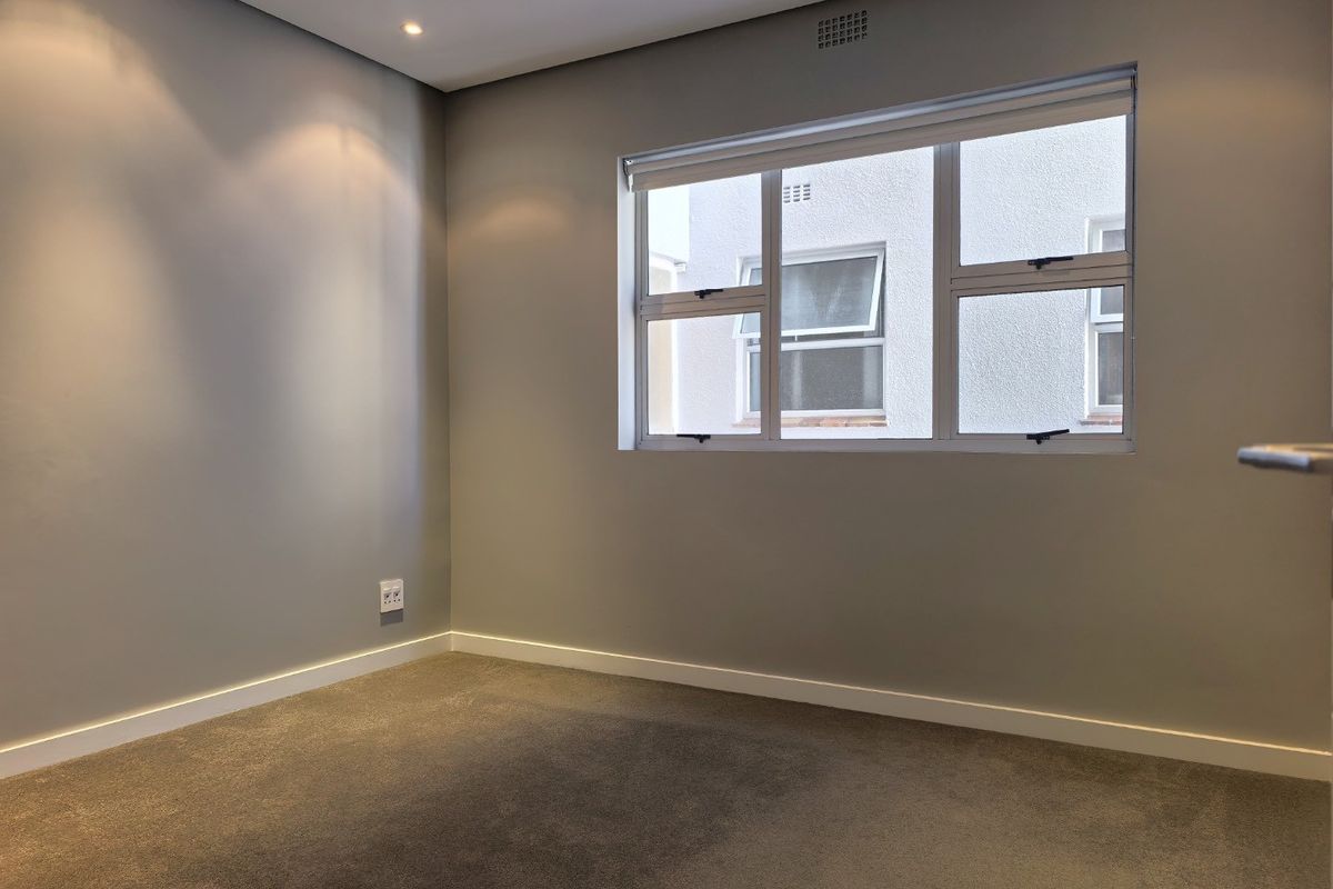 A clean, empty bedroom featuring neutral grey walls, plush carpeting, and modern aluminium-framed windows with integrated ventilation.