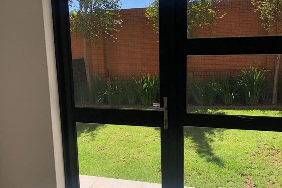 View through black-framed glass double doors looking out onto a private garden with paved patio and brick boundary wall.