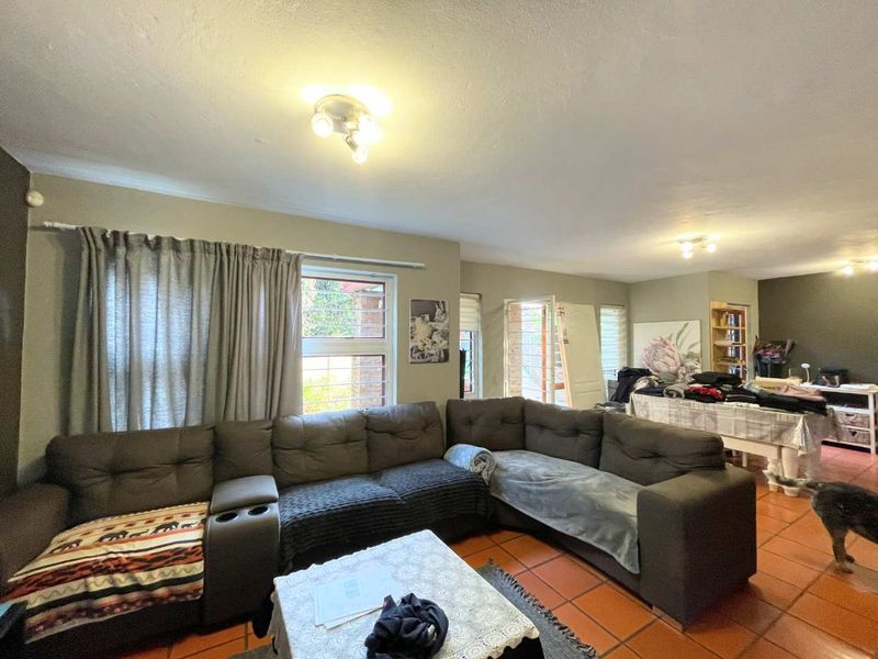 Open plan living area featuring terracotta floor tiles and security bars on windows, providing a functional space with potential for modern updates.