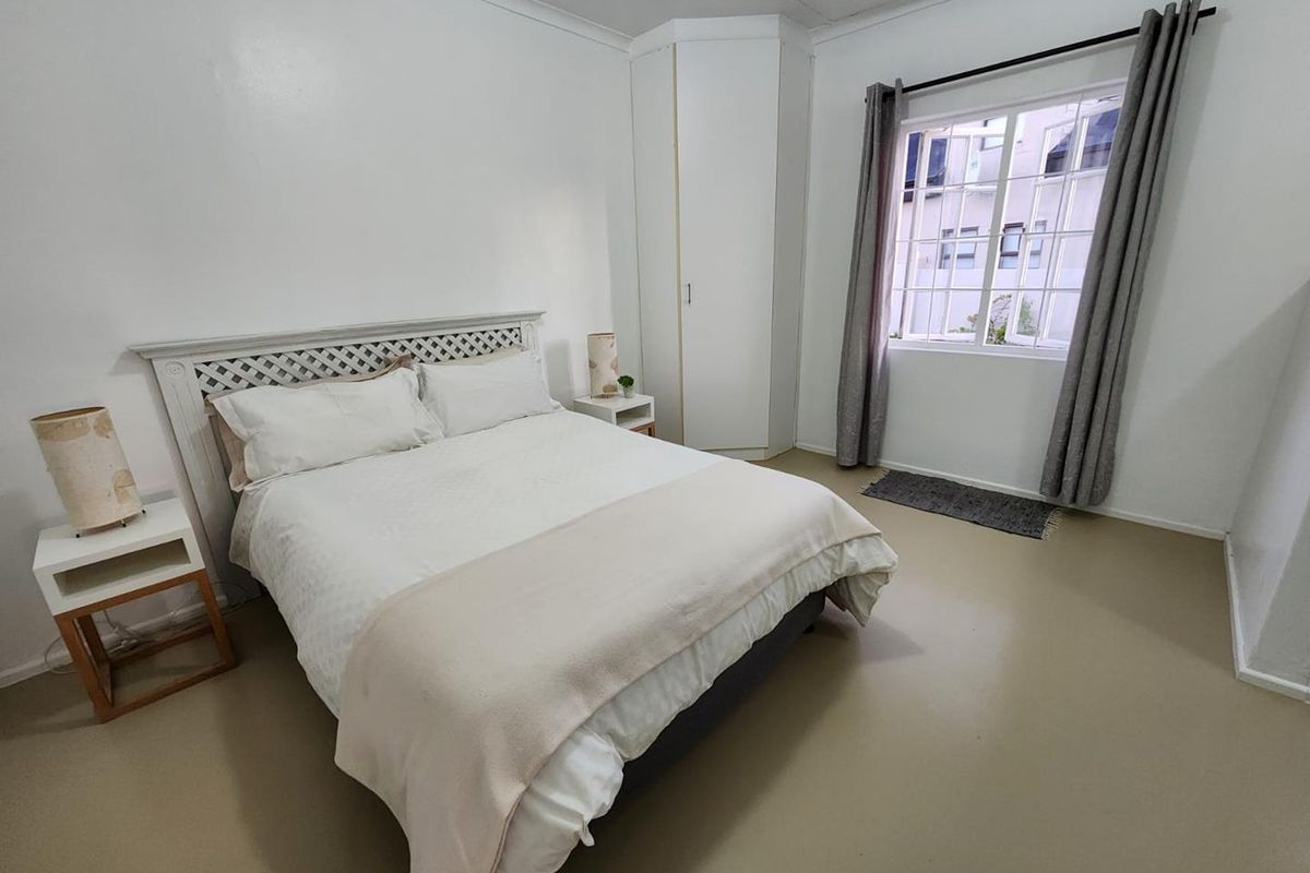 A bright bedroom featuring built-in corner cabinetry, neutral flooring, and a window with curtain tracks.