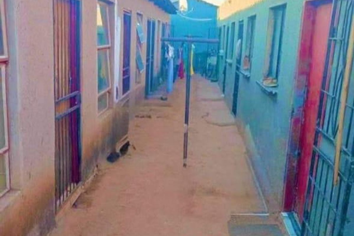 Narrow exterior corridor between two rows of residential units featuring metal security gates and basic building finishes.