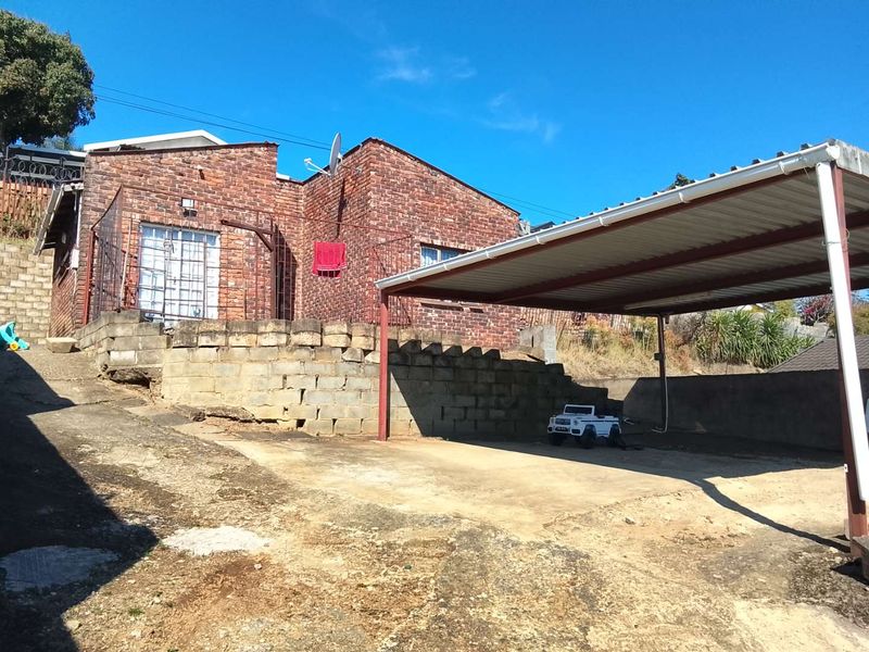 Front exterior view of a face brick house featuring a large carport, concrete driveway, and a tiered retaining wall structure.