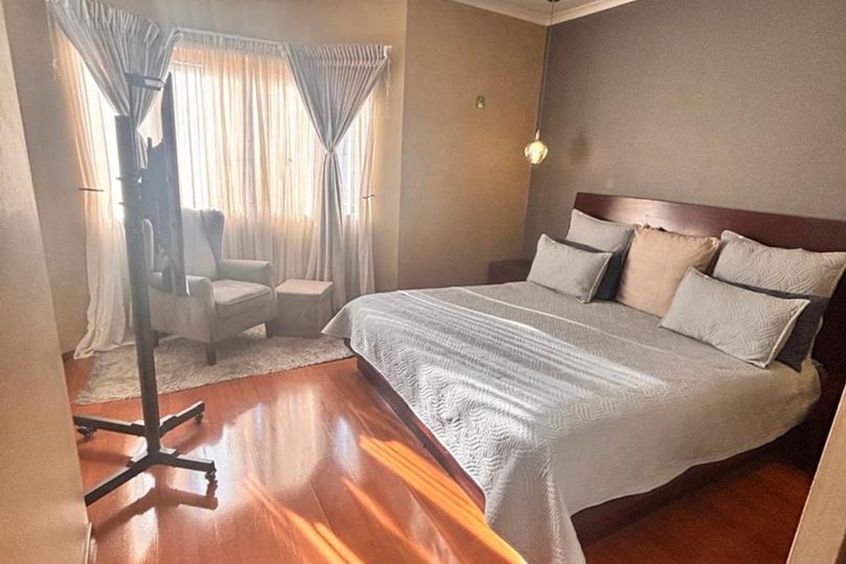 A spacious bedroom featuring warm-toned laminate flooring, neutral wall finishes, and a large window with natural light.