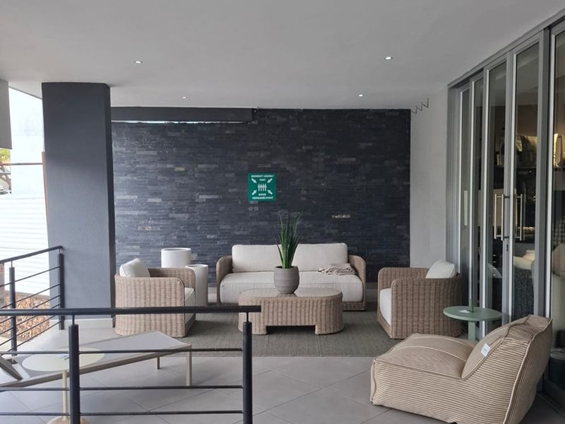 A spacious covered patio featuring modern tiled flooring, a striking stacked stone feature wall, and sleek metal balustrades, providing a seamless indoor-outdoor transition.
