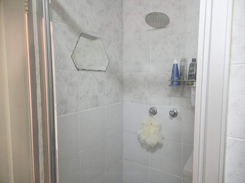 A functional shower enclosure featuring tiled walls, a fixed shower head, and a wall-mounted mixer.