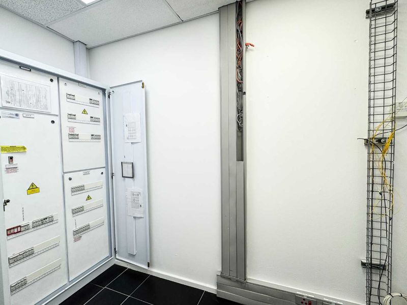 A functional utility or server room featuring a large electrical distribution board, exposed cable trunking, and wire cable tray systems.