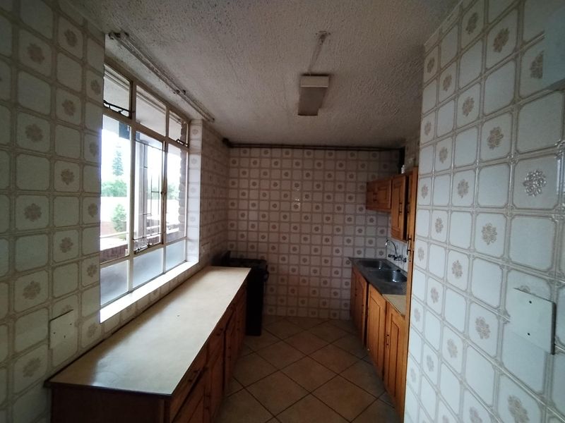 A dated kitchen featuring wooden cabinetry, double basin sink, and extensive wall tiling, offering a blank canvas for a modern renovation.