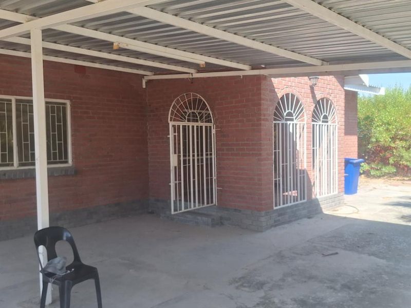 A covered outdoor patio area featuring a corrugated metal roof, brick exterior walls, and secure metal gates, providing a functional space for outdoor use.