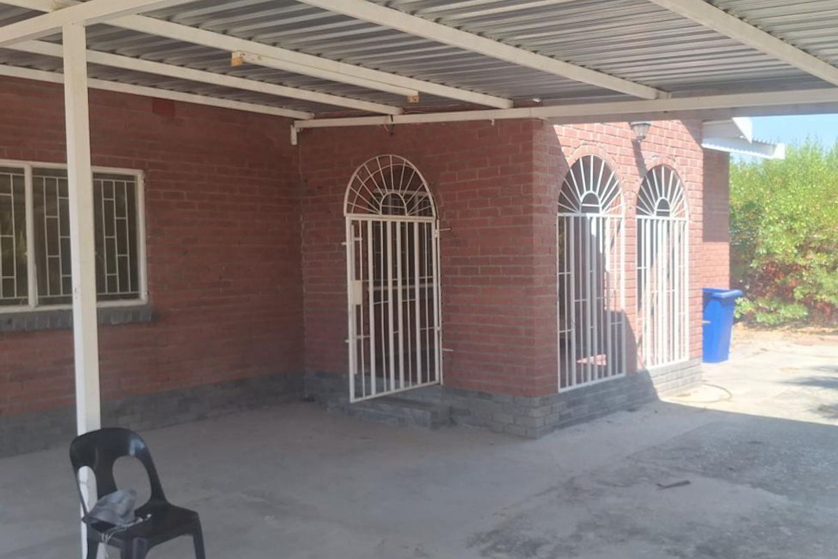 A covered outdoor patio area featuring a corrugated metal roof, brick exterior walls, and secure metal gates, providing a functional space for outdoor use.