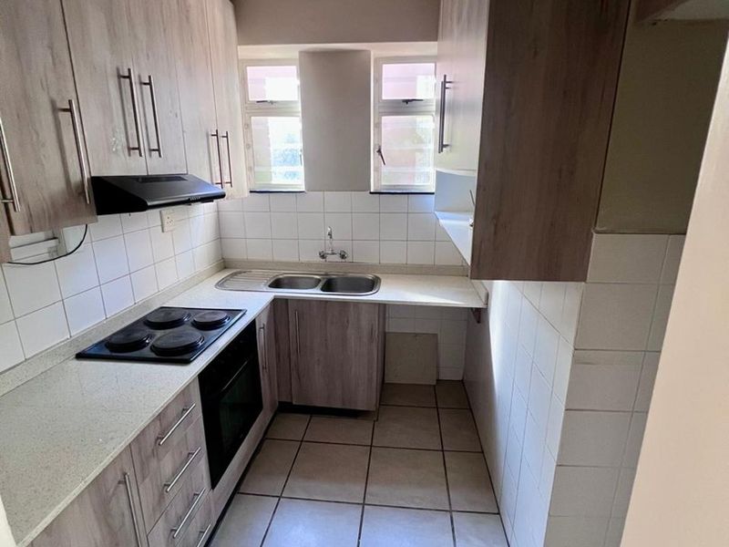 A compact, functional kitchen featuring wood-look cabinetry, laminate countertops, a built-in electric hob, oven, and tiled flooring with a neutral backsplash.