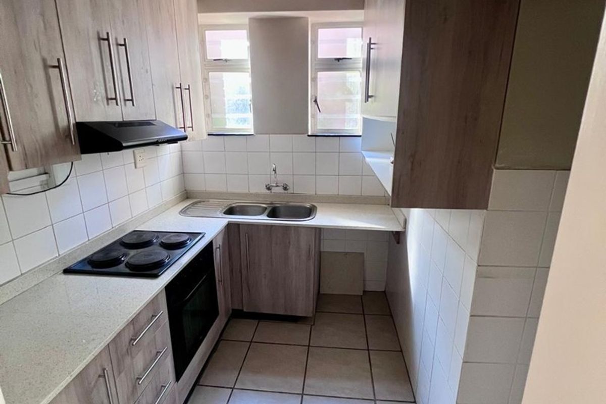 A compact, functional kitchen featuring wood-look cabinetry, laminate countertops, a built-in electric hob, oven, and tiled flooring with a neutral backsplash.