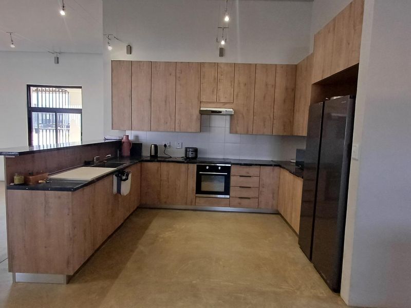 Modern open-plan kitchen featuring wood-finish cabinetry, stone countertops, integrated oven, and polished concrete flooring, seamlessly connecting to the adjacent living area.