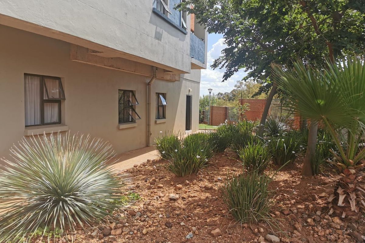 Exterior view of the apartment building featuring a landscaped garden area with established shrubs and a paved walkway along the side elevation.