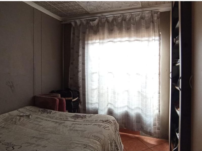A bedroom featuring built-in wardrobe storage, tiled flooring, and a textured ceiling, requiring cosmetic updates to the wall finishes.
