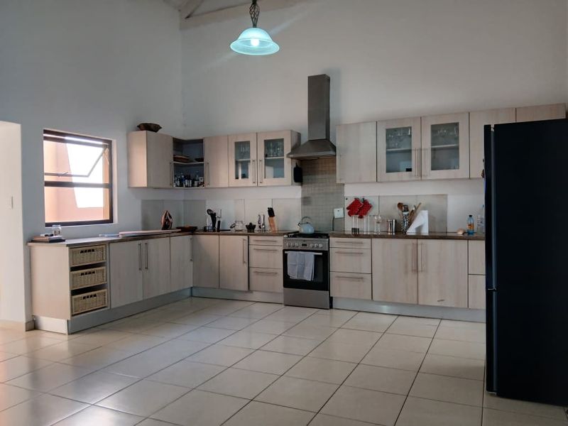 Spacious kitchen featuring light wood-finish cabinetry, stainless steel extractor fan, tiled backsplash, and neutral floor tiles with ample counter space.