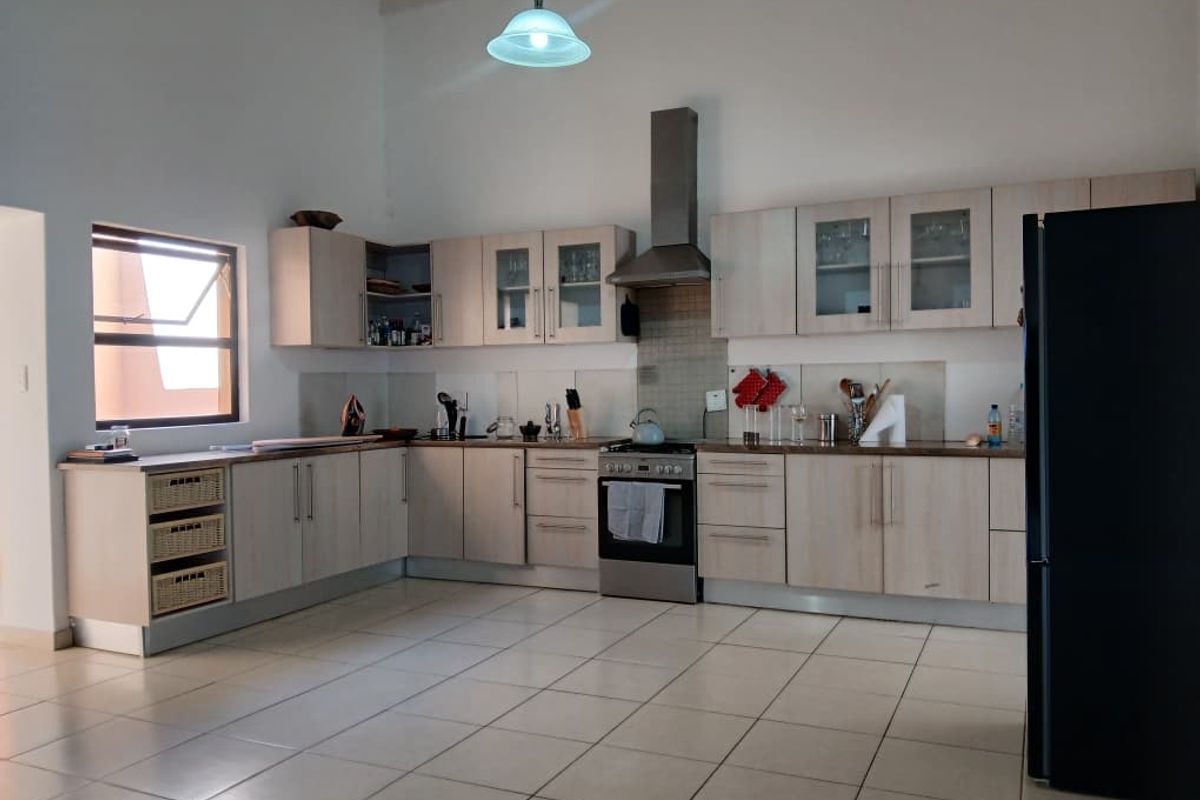 Spacious kitchen featuring light wood-finish cabinetry, stainless steel extractor fan, tiled backsplash, and neutral floor tiles with ample counter space.