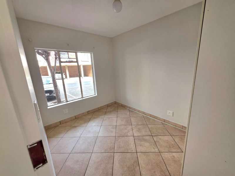 An empty bedroom featuring tiled flooring and a large window, providing a blank canvas for potential interior design and furnishing.