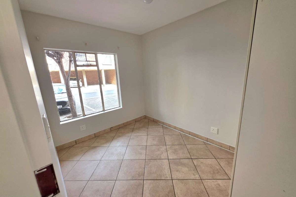 An empty bedroom featuring tiled flooring and a large window, providing a blank canvas for potential interior design and furnishing.