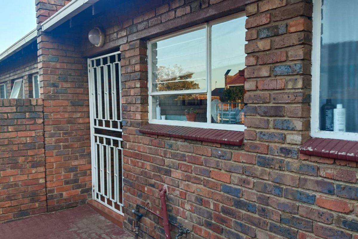 Exterior view of an apartment featuring face brick walls, security gate, and metal-framed windows with painted sills.