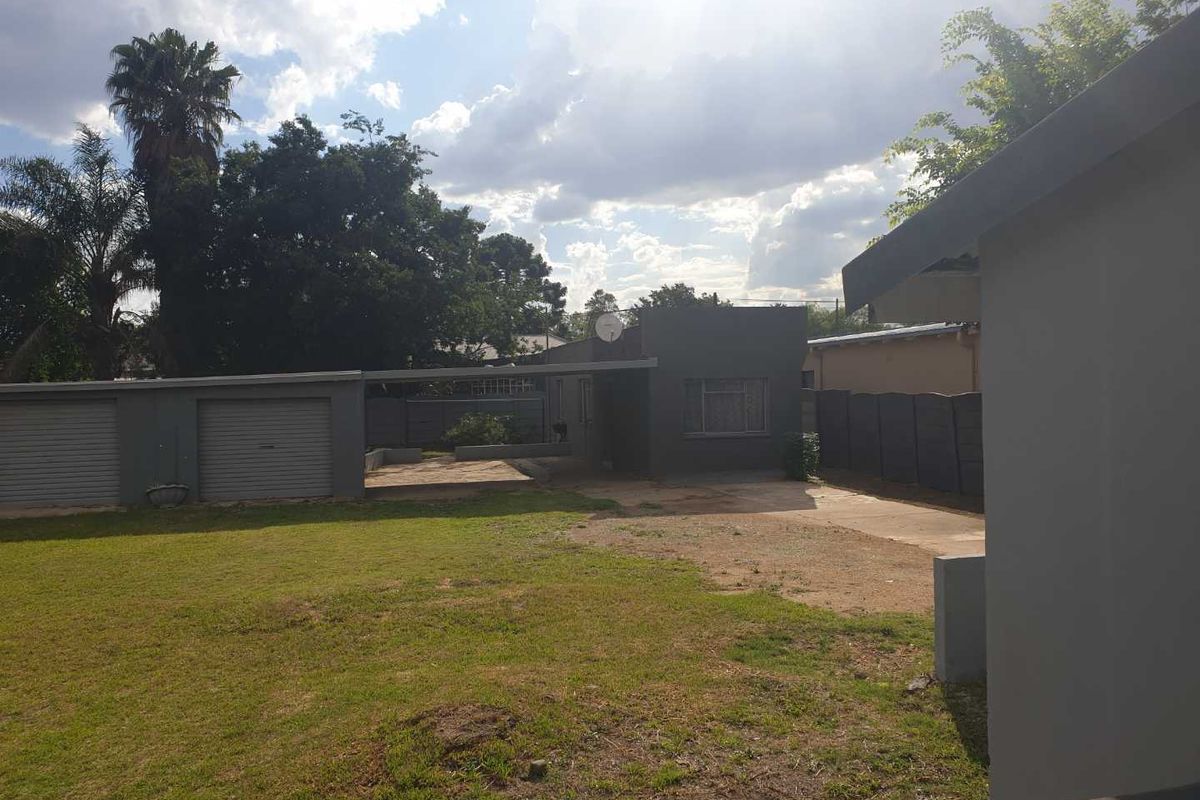 Rear view of the property featuring a double garage, concrete driveway, and a spacious lawn enclosed by precast boundary walls.