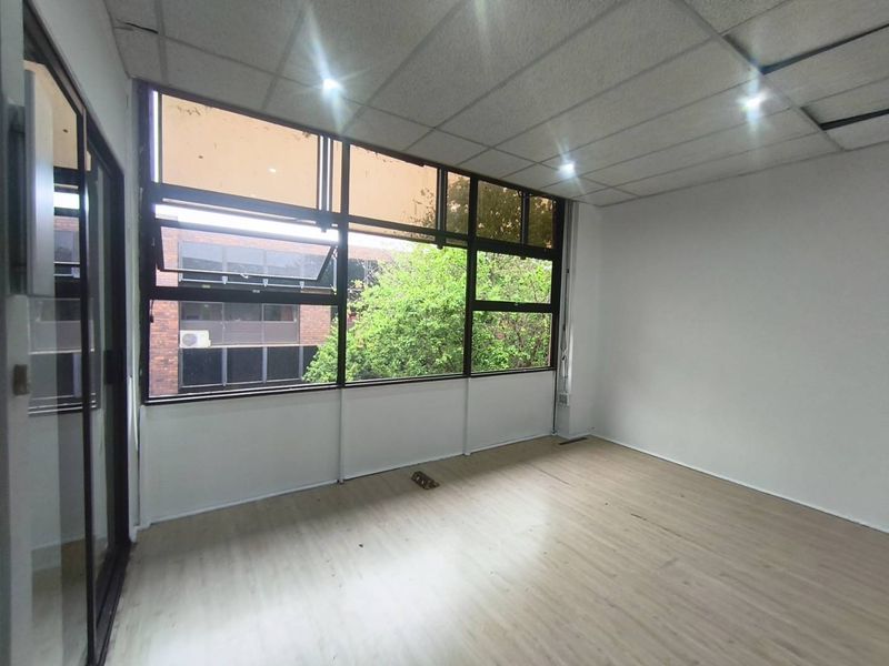 A vacant office space featuring large windows, laminate flooring, and a suspended ceiling with recessed lighting, offering a bright and functional workspace.