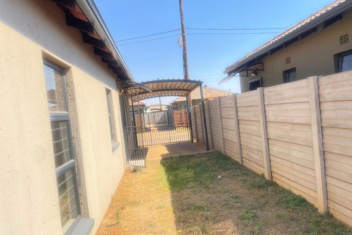 Side yard area featuring a metal carport, security gate, and precast concrete boundary wall, providing a functional outdoor space.