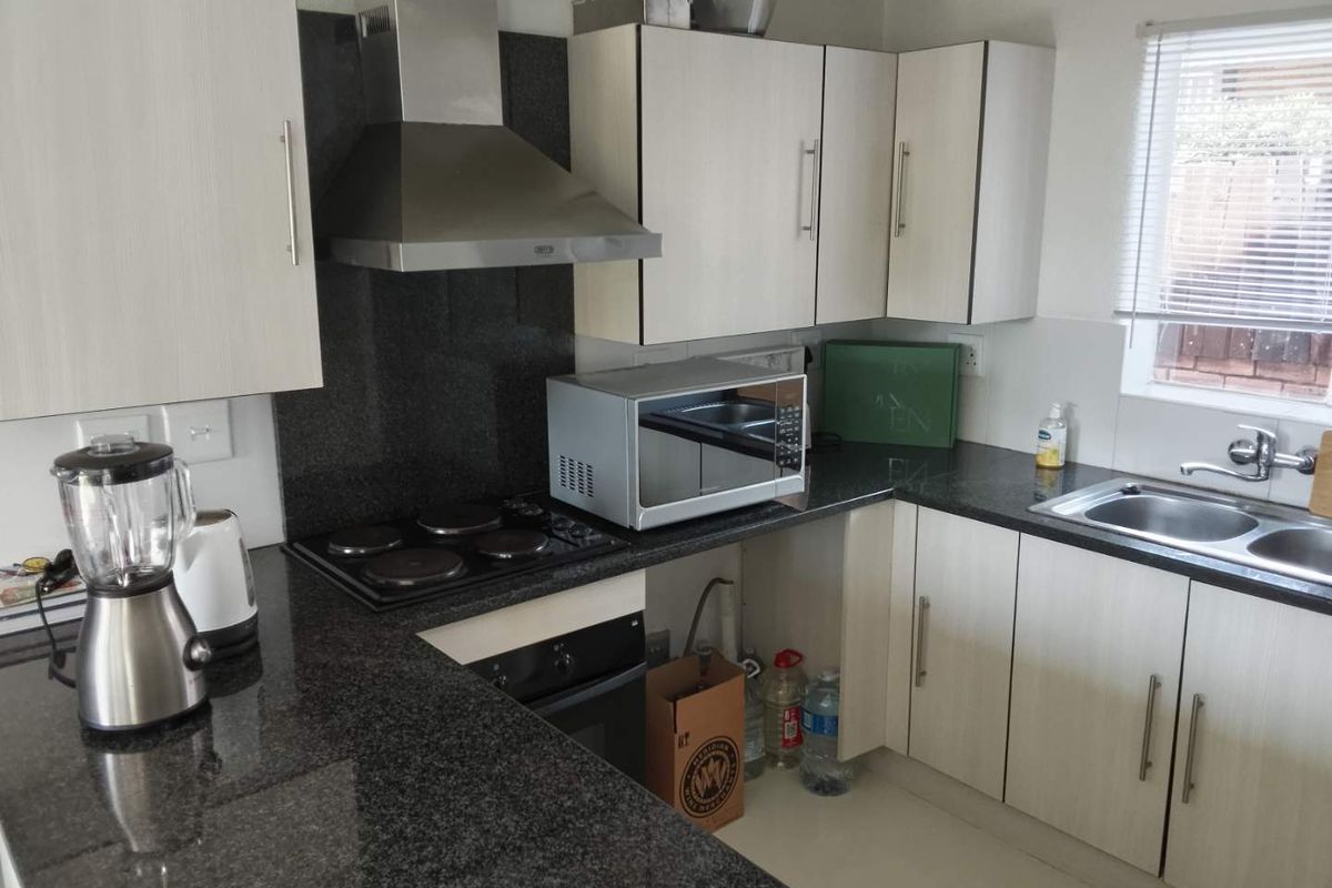 Functional kitchen featuring granite countertops, built-in oven, electric hob, stainless steel extractor fan, and ample laminate cabinetry with a double bowl sink.