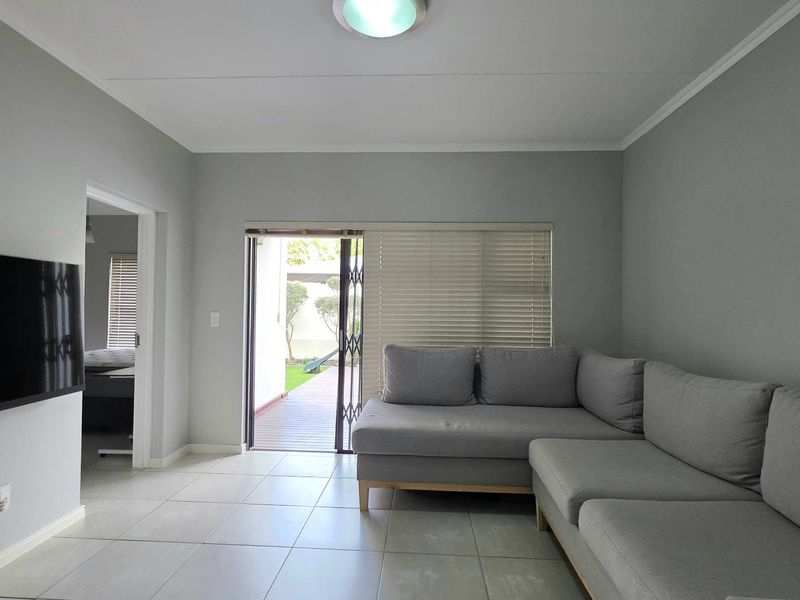 A bright living room featuring neutral tiled flooring, a sliding door with security gate leading to an outdoor area, and clean wall finishes.