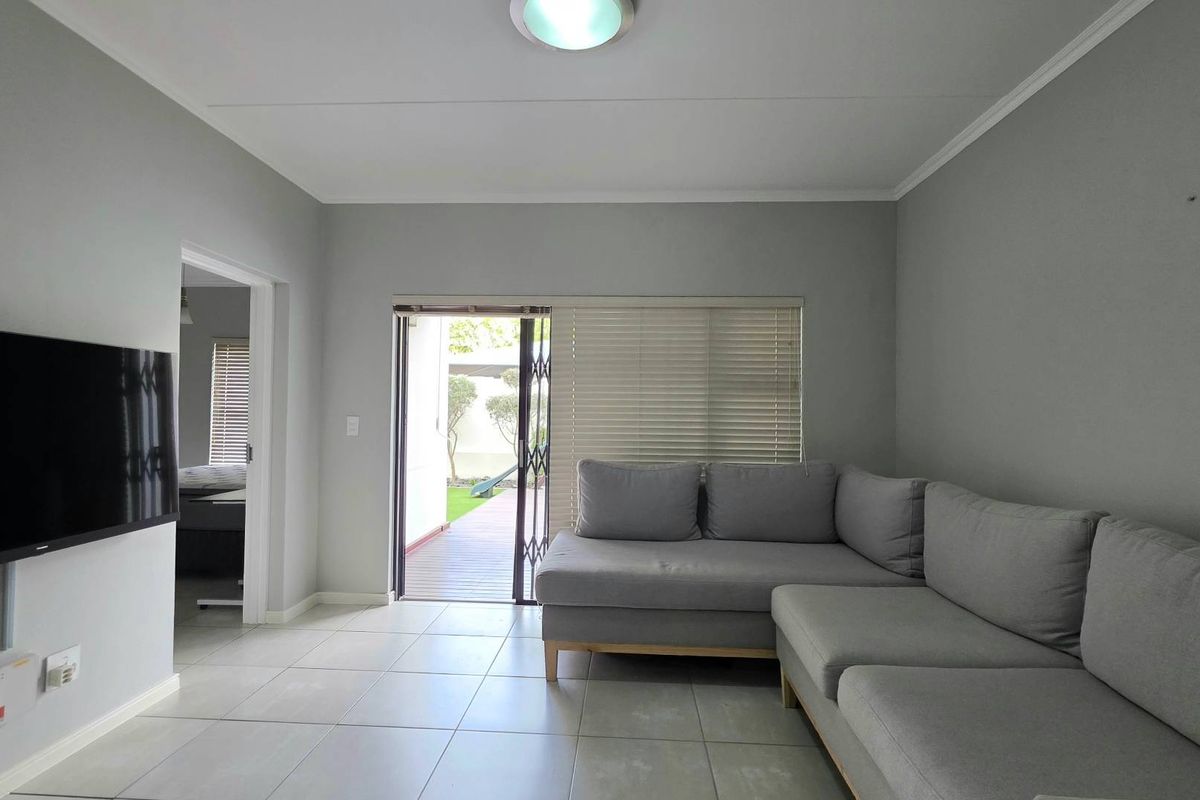 A bright living room featuring neutral tiled flooring, a sliding door with security gate leading to an outdoor area, and clean wall finishes.