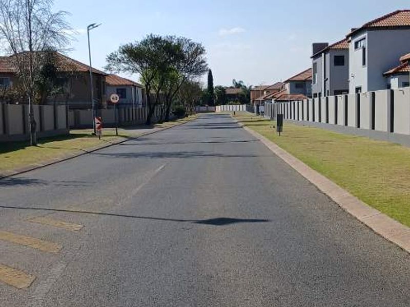 A view of the residential street within the estate, featuring paved roads, sidewalks, and perimeter walling.