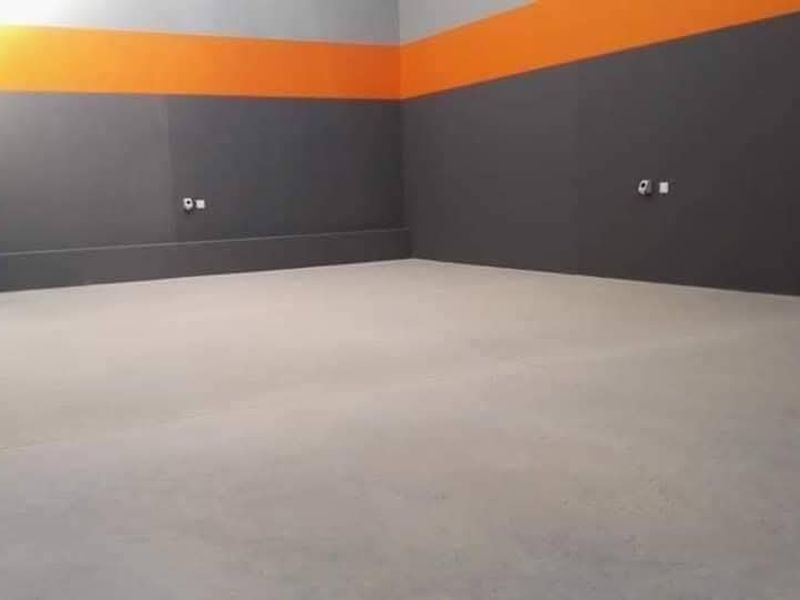 A spacious, empty industrial utility area featuring smooth concrete flooring, painted walls with high-visibility accents, and integrated electrical power points.