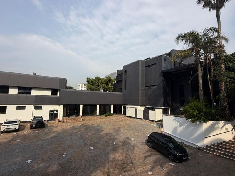 A view of the rear courtyard featuring paved parking, modern dark metal cladding, and a covered walkway connecting the building sections.