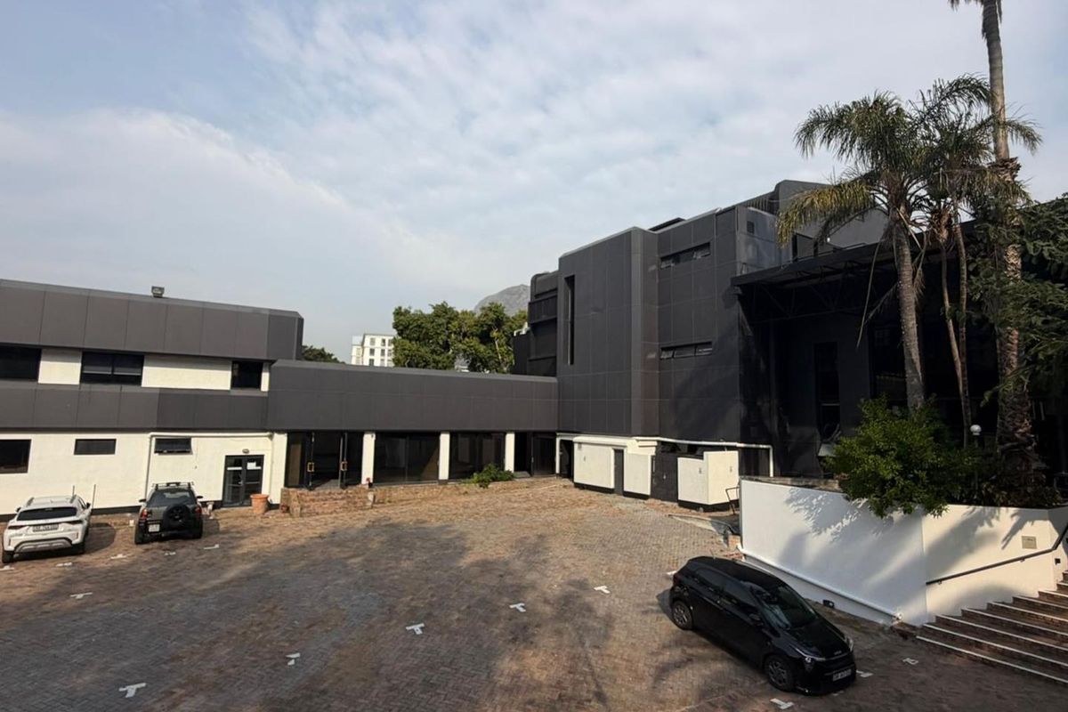 A view of the rear courtyard featuring paved parking, modern dark metal cladding, and a covered walkway connecting the building sections.